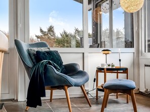 Une chambre moderne avec une grande fenêtre, un fauteuil bleu, une petite table avec une lampe et une bougie.