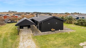 A black metal building with a gravel driveway and a small covered area.