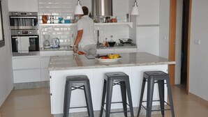 Una cucina moderna con mobili bianchi, un forno in acciaio inossidabile, una macchina da caffè e una ciotola di frutta sull'isola.
