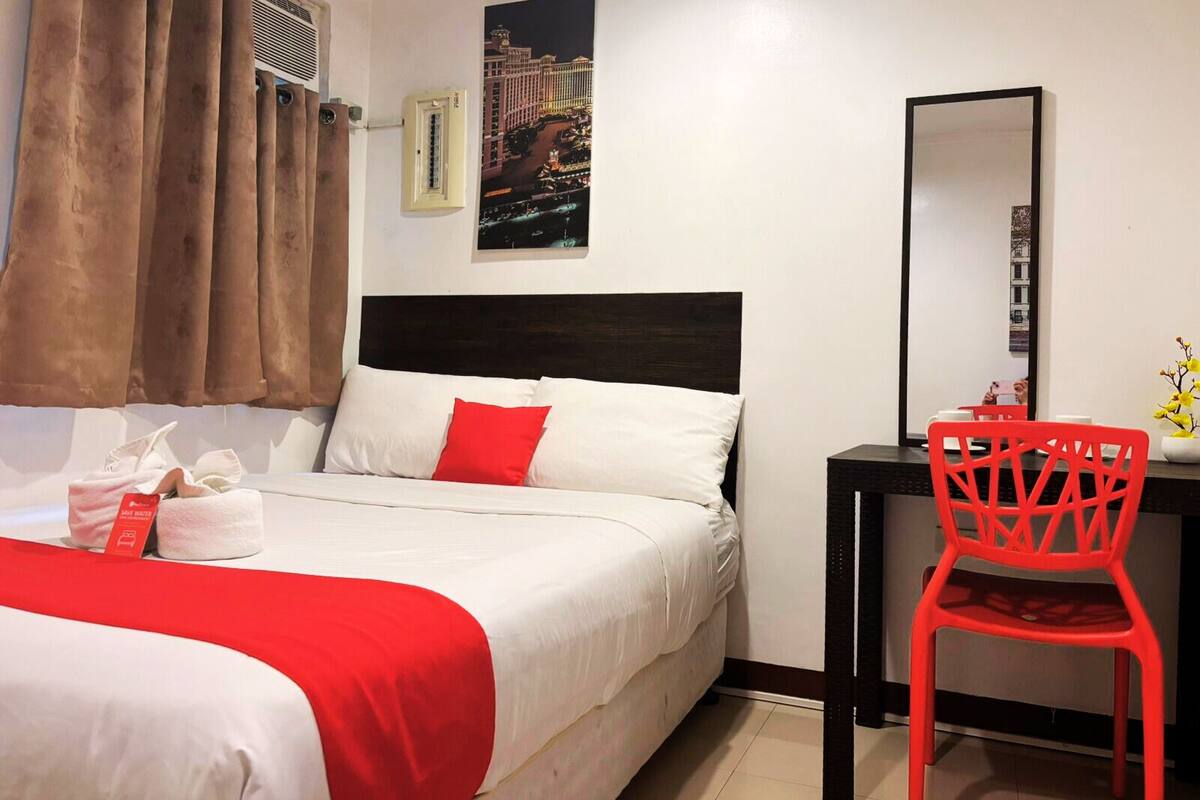 Habitación de hotel con cama, escritorio, silla, espejo y aire acondicionado instalado en la pared.