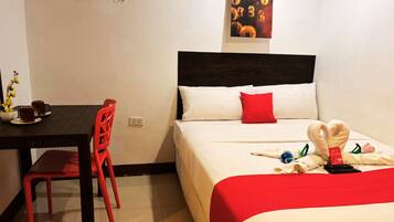 Habitación de hotel con cama, escritorio con silla, una mesita con un jarrón de flores y un cuadro colgado en la pared.