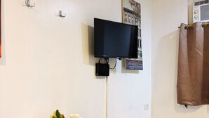 Un coin repas avec une table noire, une chaise rouge, deux tasses blanches, un cactus et un téléviseur fixé au mur.