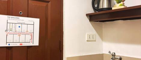 Una cocina con un lavamanos, una cafetera y un plano de evacuación contra incendios en la puerta.