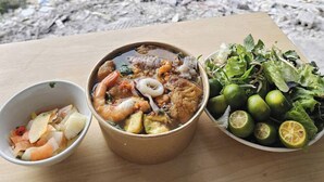 A meal with seafood and vegetables, a bowl of greens, and limes on a table by a river. - ZingHome Ha Giang (Ha Giang 1)
