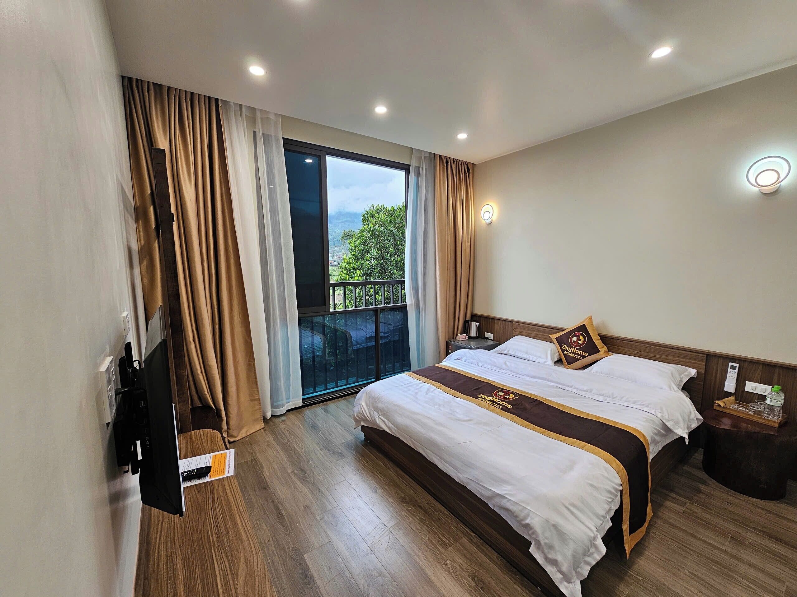 A hotel room with a large bed, a TV, a bedside table, and a view of the outdoors.