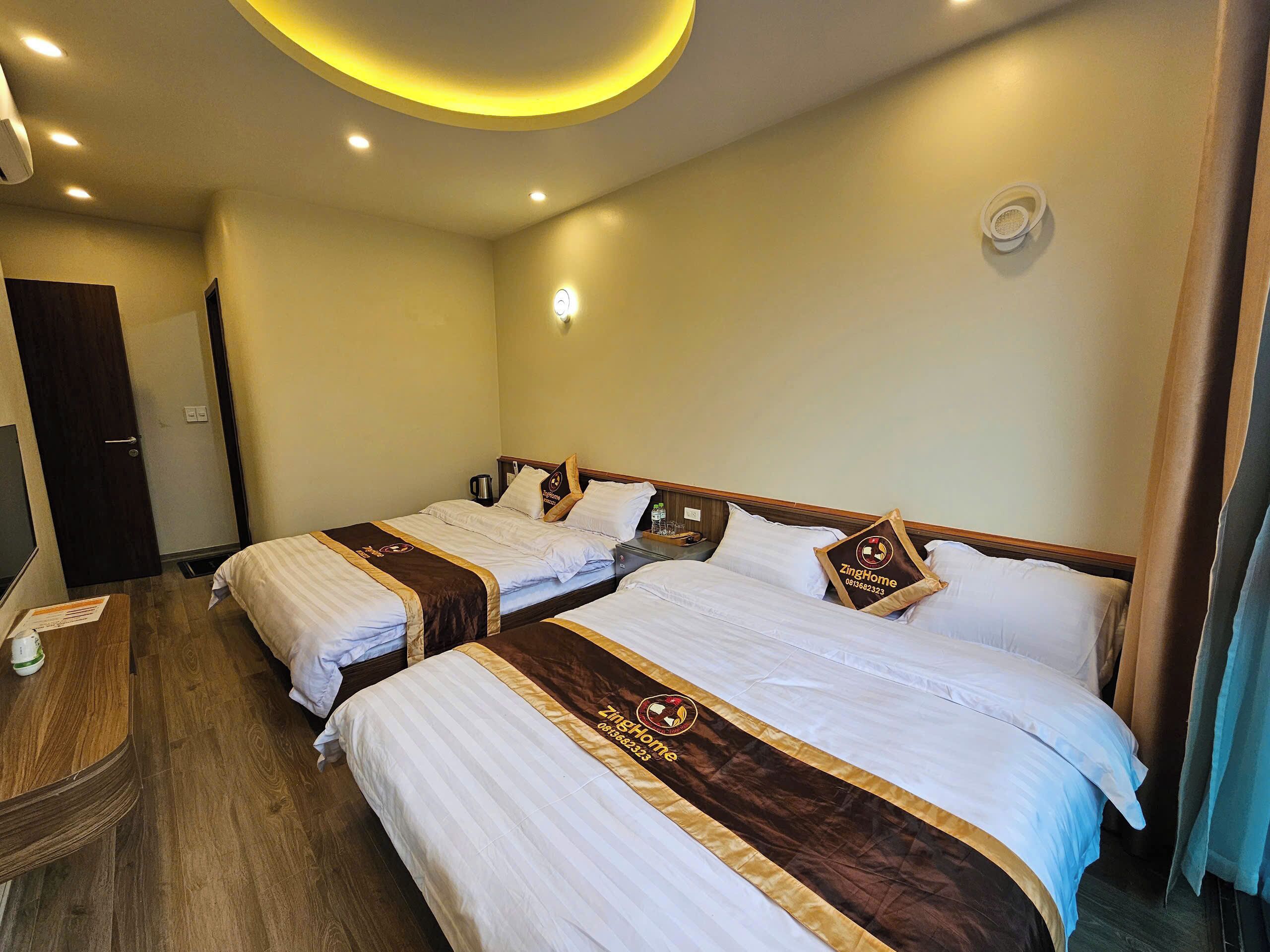 A hotel room with two beds, a wooden nightstand, a desk, and a door.
