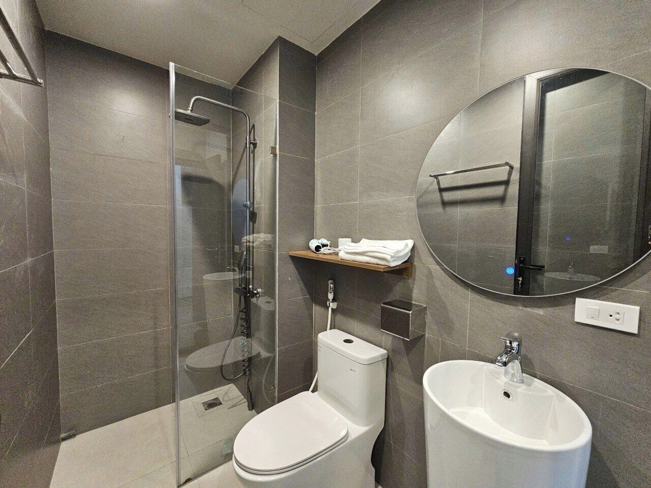 Un baño moderno con ducha envuelta en vidrio, inodoro y lavabo con espejo sobre él.