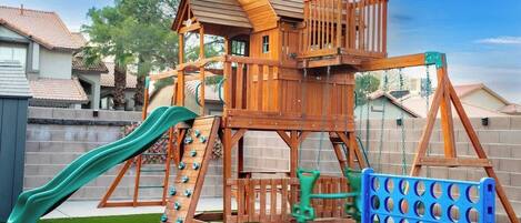 A wooden play structure with a slide, climbing ladder, and swings.