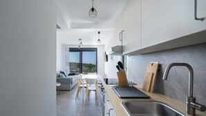 A modern kitchen with a large window, a dining area with a white table and chairs, and a view of greenery outside. - Villa Artec with Sea View and Private Pool (Marcana)