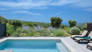 A swimming pool with lounge chairs, surrounded by lush greenery and a view of the sea. - Villa Artec with Sea View and Private Pool (Marcana)