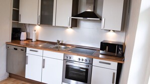 A compact kitchen with white cabinets, a stainless steel oven, a microwave, and a wooden countertop.