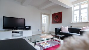 A modern living room with a flat-screen TV, a glass coffee table, a black leather sofa, and a red abstract painting on the wall.