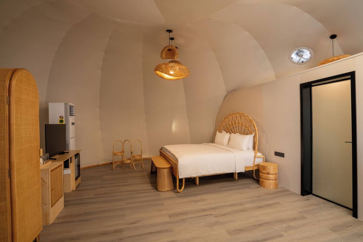 A compact bedroom with a bed, bedside tables, a TV, and a small kitchenette.