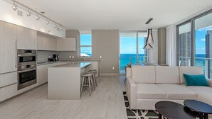 Une cuisine moderne dotée d’appareils électroménagers intégrés, d’un îlot central avec des tabourets et d’une grande fenêtre donnant sur l’océan.