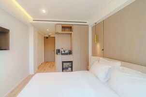 A modern hotel room with a large bed, a built-in wardrobe, a minibar, and a flat-screen TV mounted on the wall.