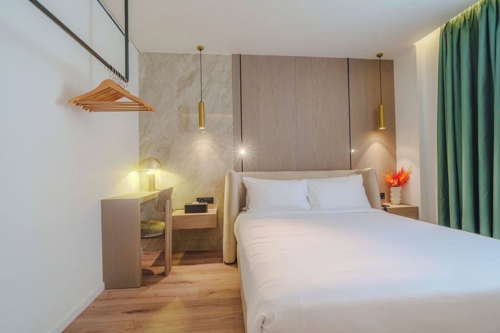 Una camera d'albergo moderna con un letto grande, una testiera in legno, una scrivania con una sedia e due lampade a sospensione.