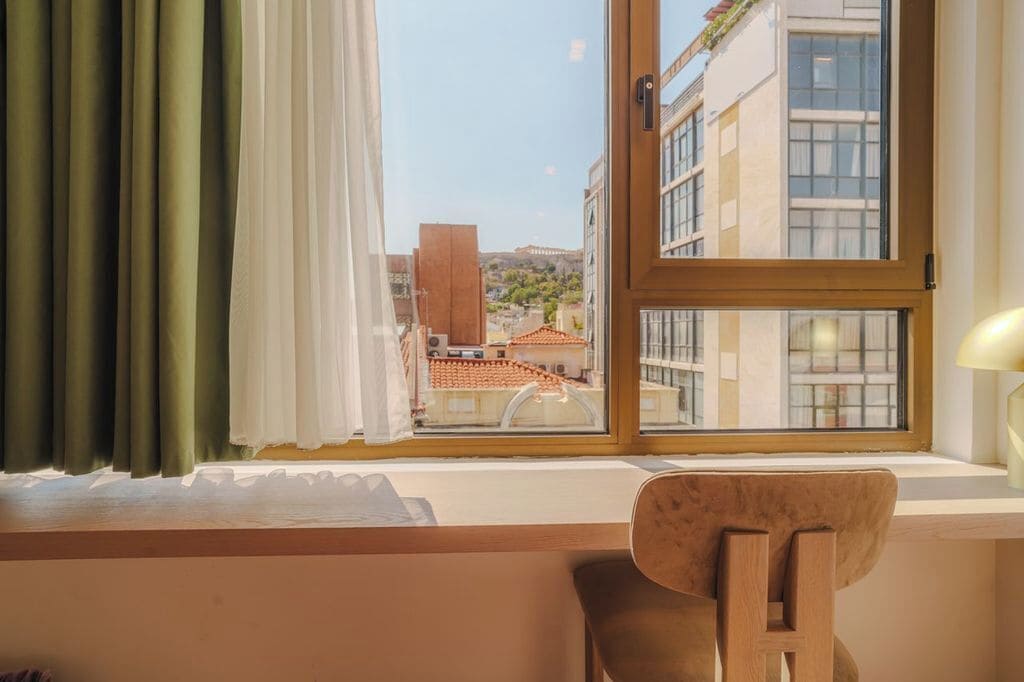 A room with a view of buildings and a chair by the window.