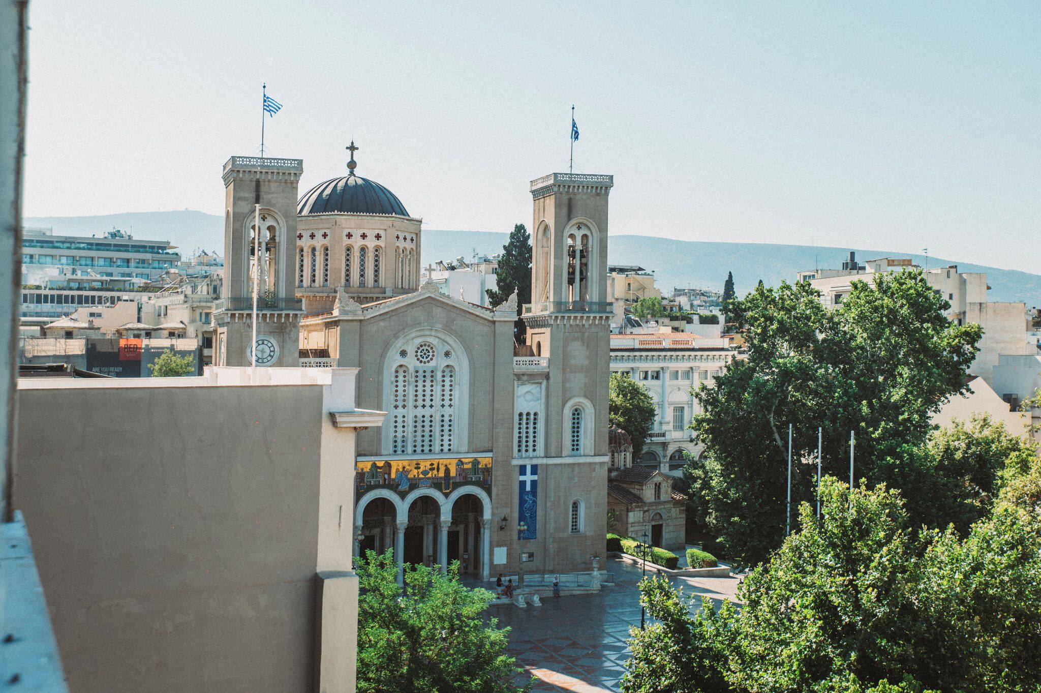 A historic church with a central dome and two bell towers, surrounded by trees and urban buildings.