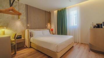 Quarto de hotel moderno com cama, mesa de cabeceira, abajur e escrivaninha com cadeira.