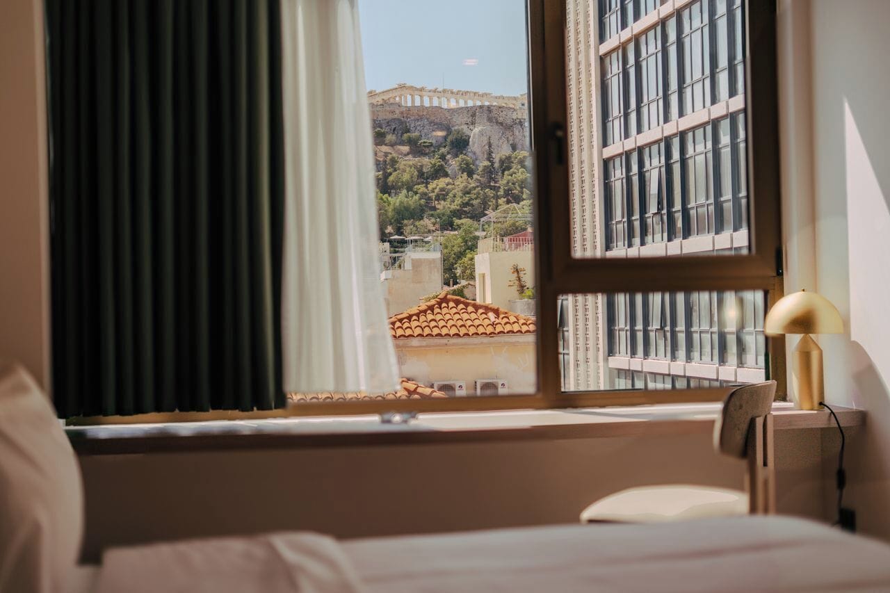 A hotel room with a large window offering a view of a historic building and a hill.