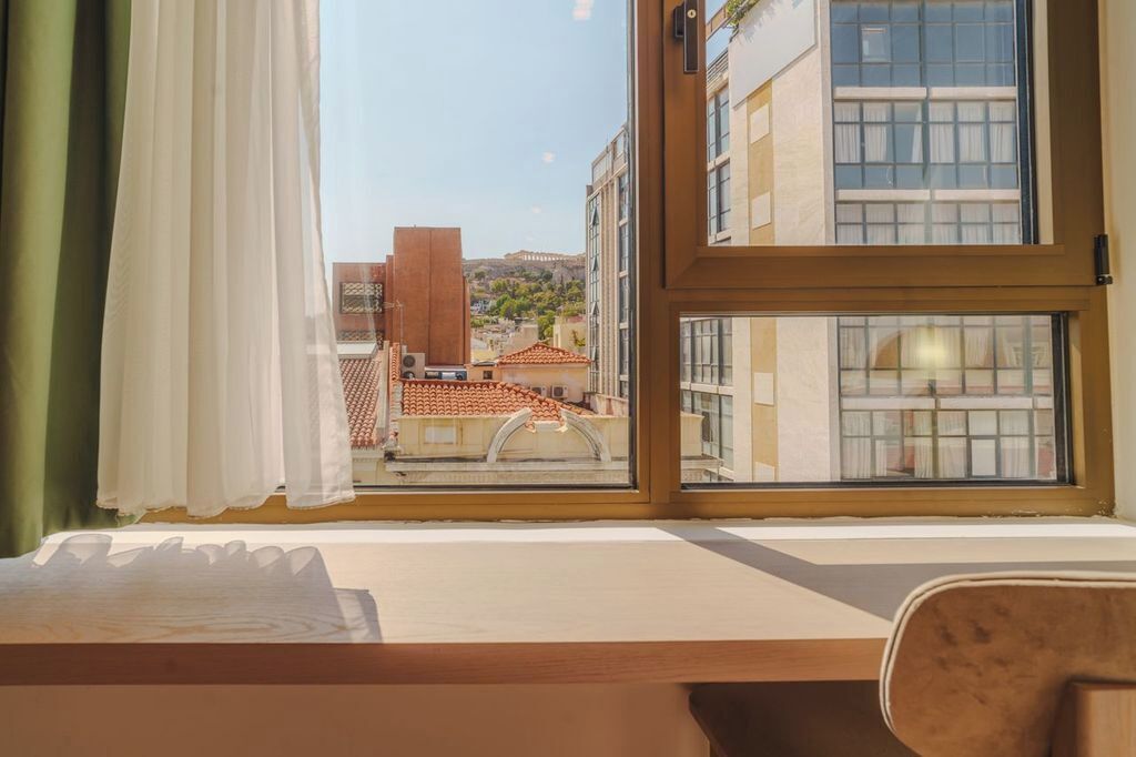 Habitación de hotel con un ventanal grande con vistas a un paisaje urbano, una cama y un cabecero de madera.
