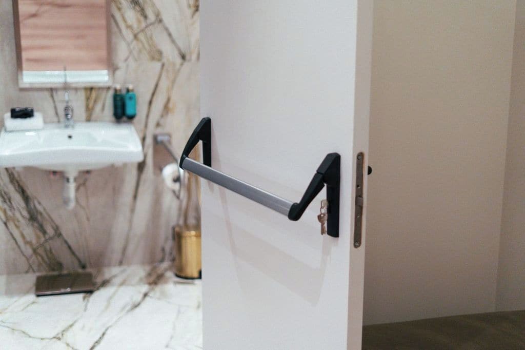 A bathroom with a white sink, a marble wall, and a door with a black handle.