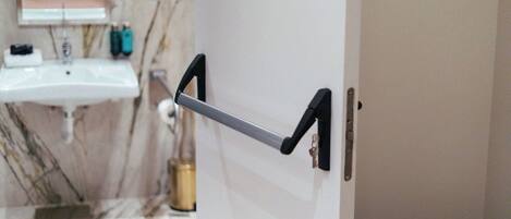 A bathroom with a white sink, a marble wall, and a door with a black handle.