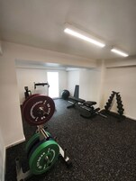 A gym with weightlifting equipment, a bench, and a wall-mounted rack.