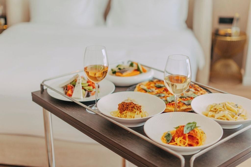 Ein Tablett mit Pasta-Tellern und einem Weinglas auf einem Tisch in einem Hotelzimmer.