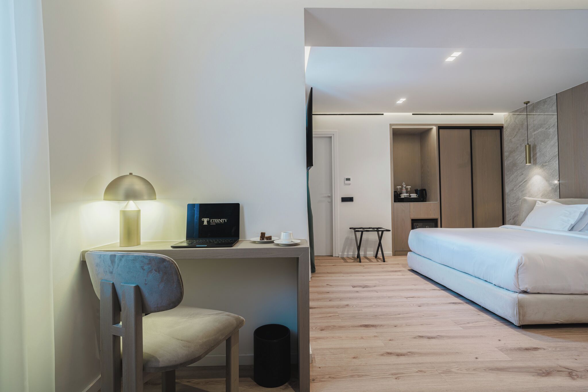 A modern hotel room with a desk, chair, laptop, and a bed.