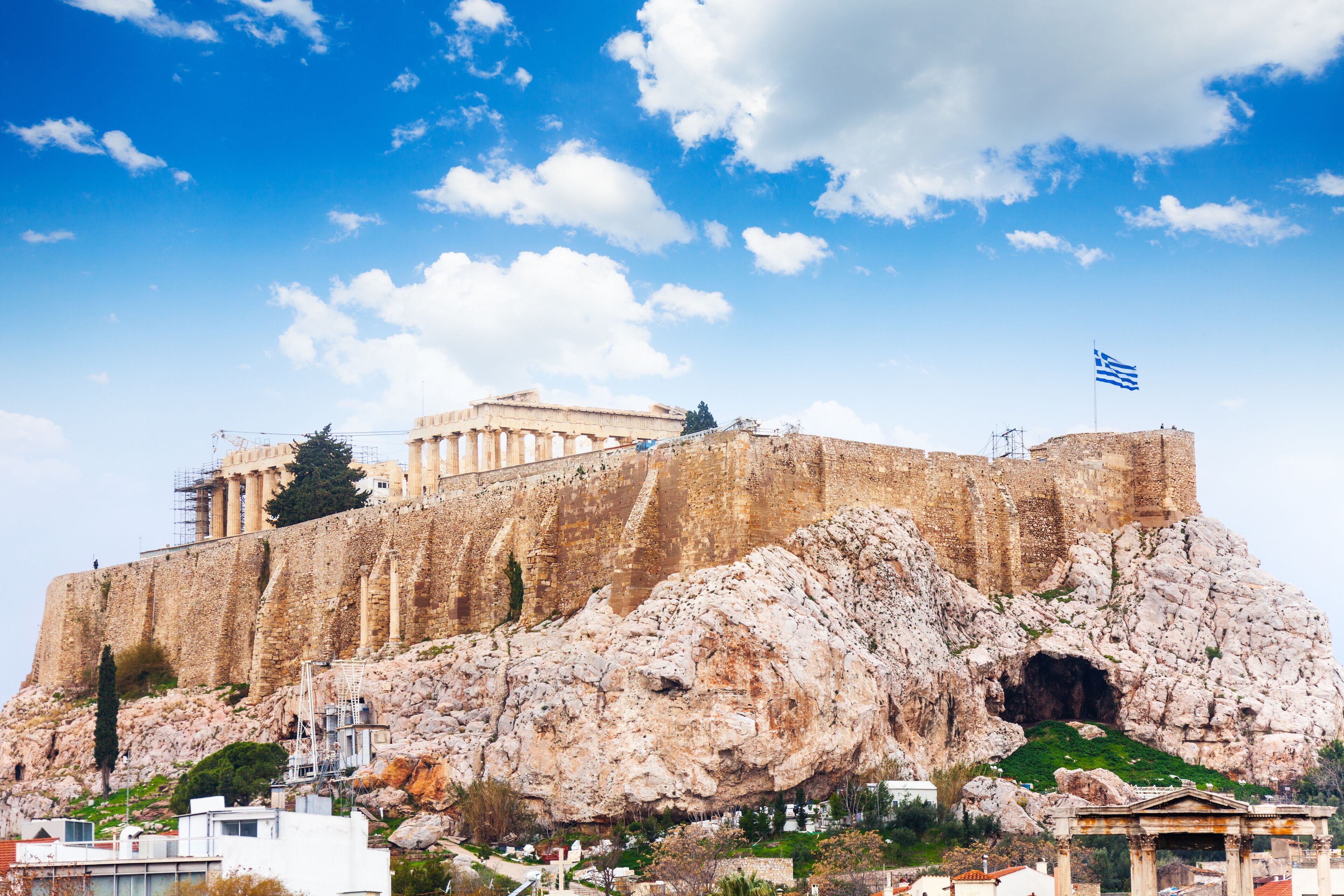 A historic building with columns, a flag, and a rocky base.