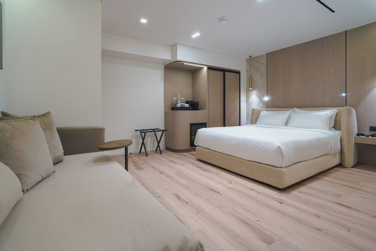 A modern bedroom with a large bed, a sofa, a small table, and built-in storage.