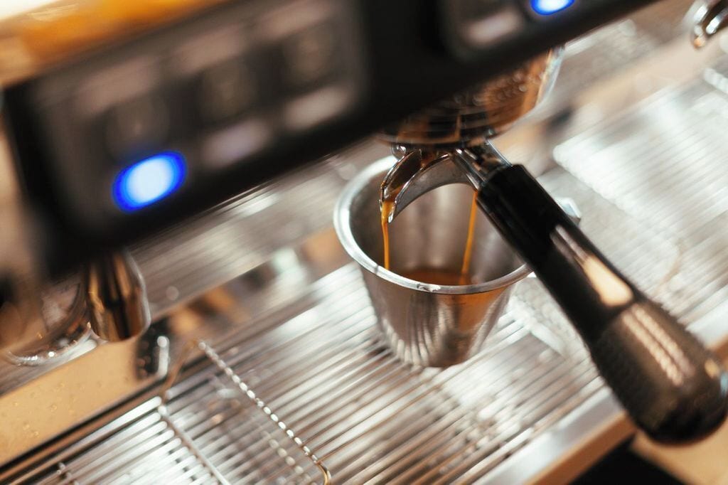 A close-up of a coffee machine dispensing espresso into a metal cup.
