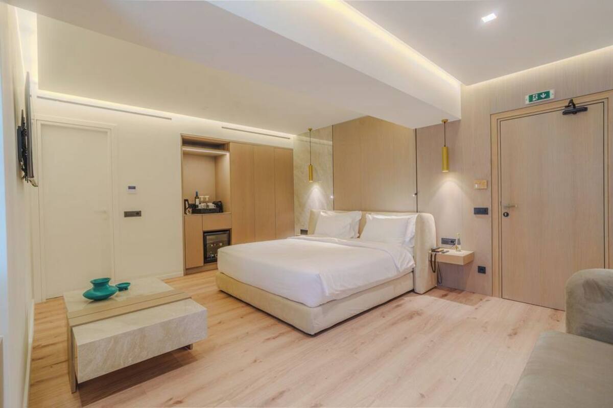 A modern bedroom with a large bed, bedside tables, a built-in wardrobe, and a small seating area.