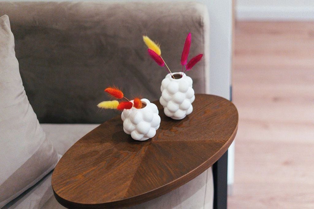 Two white ceramic vases with colorful feathers on a wooden side table.