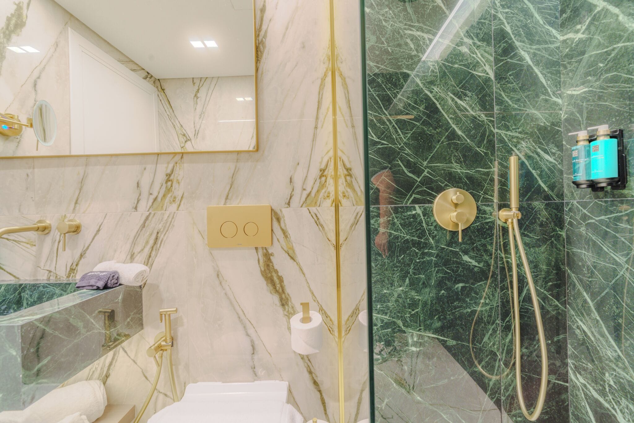 Un bagno con un vanità in marmo, cabina doccia in vetro e rubinetteria dorata.