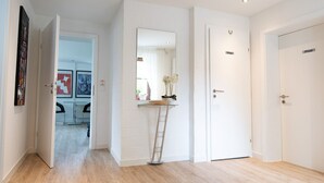 Un pasillo con paredes blancas, suelo de madera y una mesa consola de vidrio con una planta. Hay puertas con la etiqueta "Privat" y un espejo en la pared.