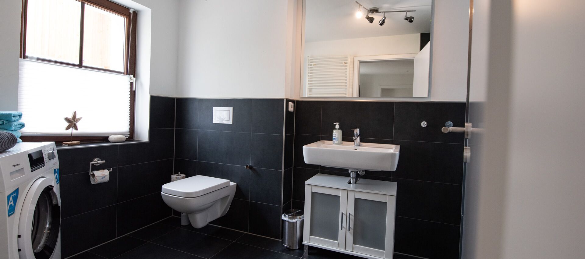 Un baño pequeño con lavadora, inodoro y lavamanos con gabinete.