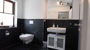 Un baño pequeño con lavadora, inodoro y lavamanos con gabinete.
