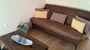 Una sala de estar con un sofá marrón, cojines estampados, una mesa de centro de madera y un cuadro en la pared.