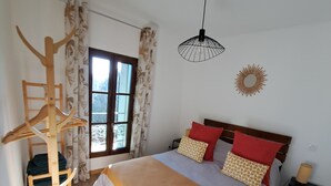 Un dormitorio con una cama grande, suelo de madera, una ventana con cortinas, una lámpara colgante y un adorno en la pared.