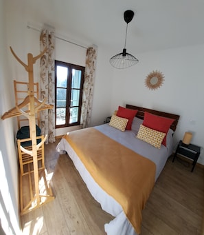 Una camera da letto con un letto grande, pavimento in legno, una finestra con tende, un lampadario e una decorazione a parete.