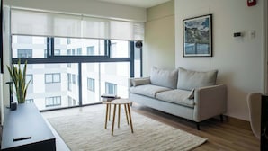 Ein modernes Wohnzimmer mit einer Couch, einem kleinen Tisch und einem großen Fenster mit Blick auf Gebäude.
