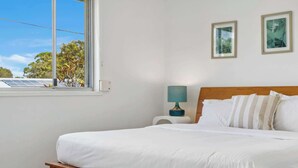 A bedroom with a bed, a nightstand, a lamp, and framed pictures on the wall. - Tides & Tails Abode - Coolum Dog Friendly Home (Coolum Region)