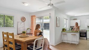 A modern kitchen with white cabinets, a wooden dining table, and a bar area. - Tides & Tails Abode - Coolum Dog Friendly Home (Coolum Region)