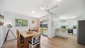 A modern kitchen with white cabinets, a dining area with a wooden table and chairs, and a ceiling fan. - Tides & Tails Abode - Coolum Dog Friendly Home (Coolum Region)