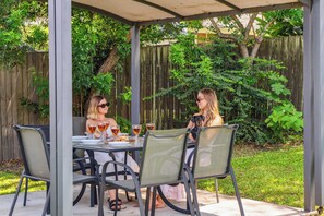 An outdoor patio with a table and chairs, surrounded by a wooden fence and greenery.