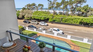 Un balcon avec une piscine, un espace repas et une vue sur la rue et l  ’océan.