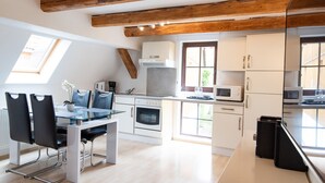 Een moderne keuken met witte kasten, een inbouwoven en een magnetron. Er is een eethoek met een glazen tafel en stoelen.