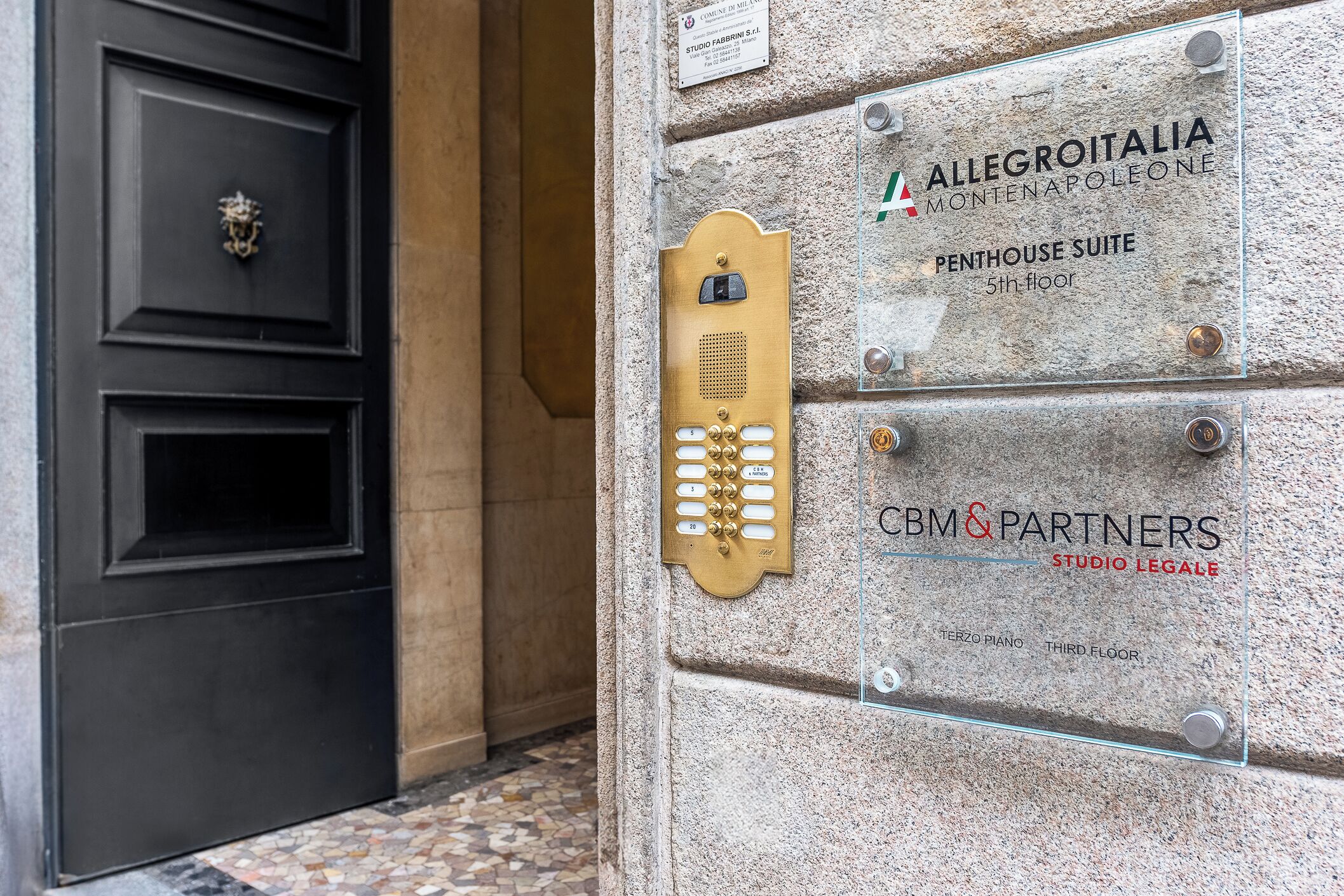 A building entrance with a black door, a brass intercom, and a sign indicating the Penthouse Suite on the 5th floor.